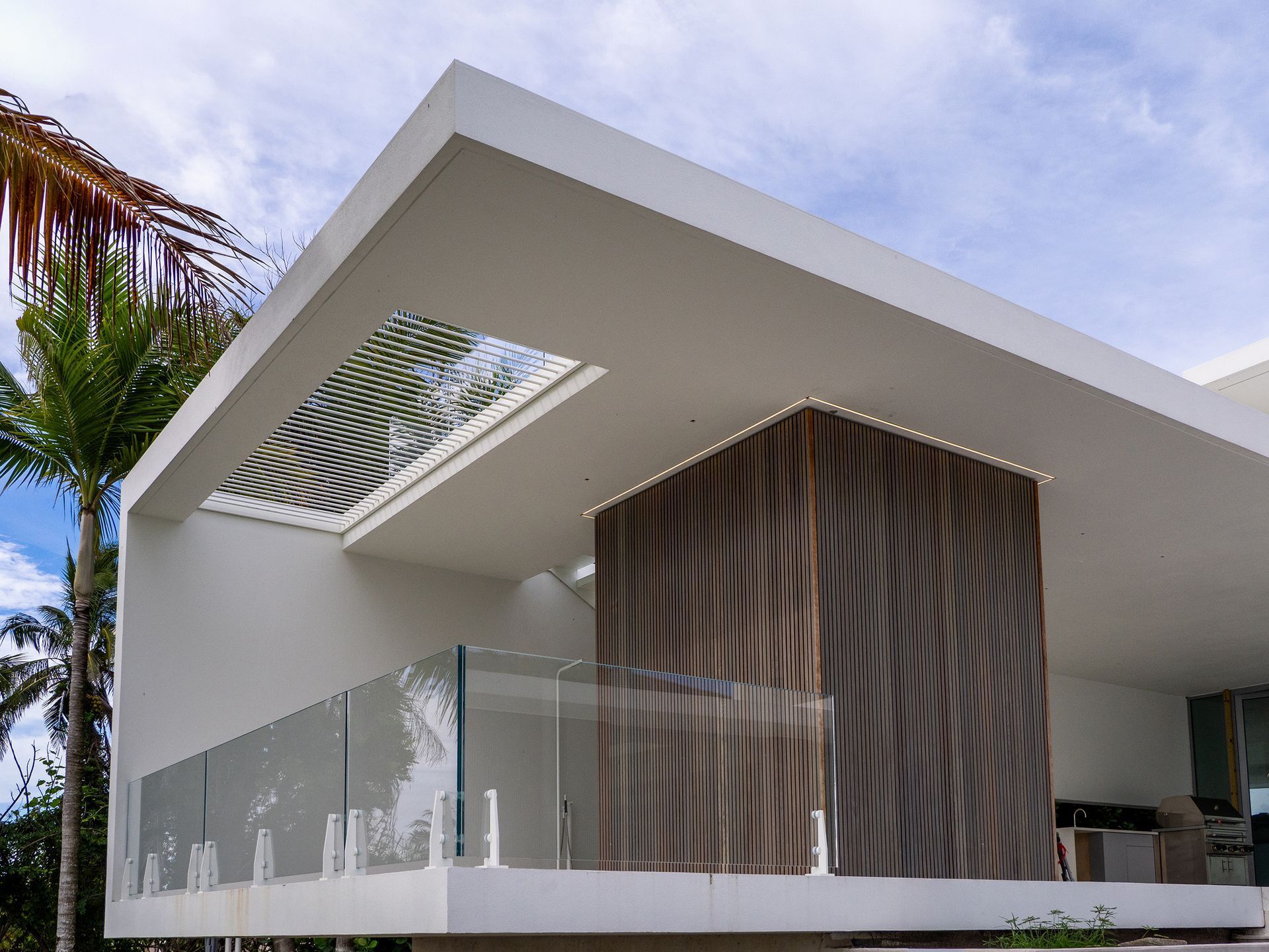 Modern white house with glass railing, wooden accent, and a skylight.