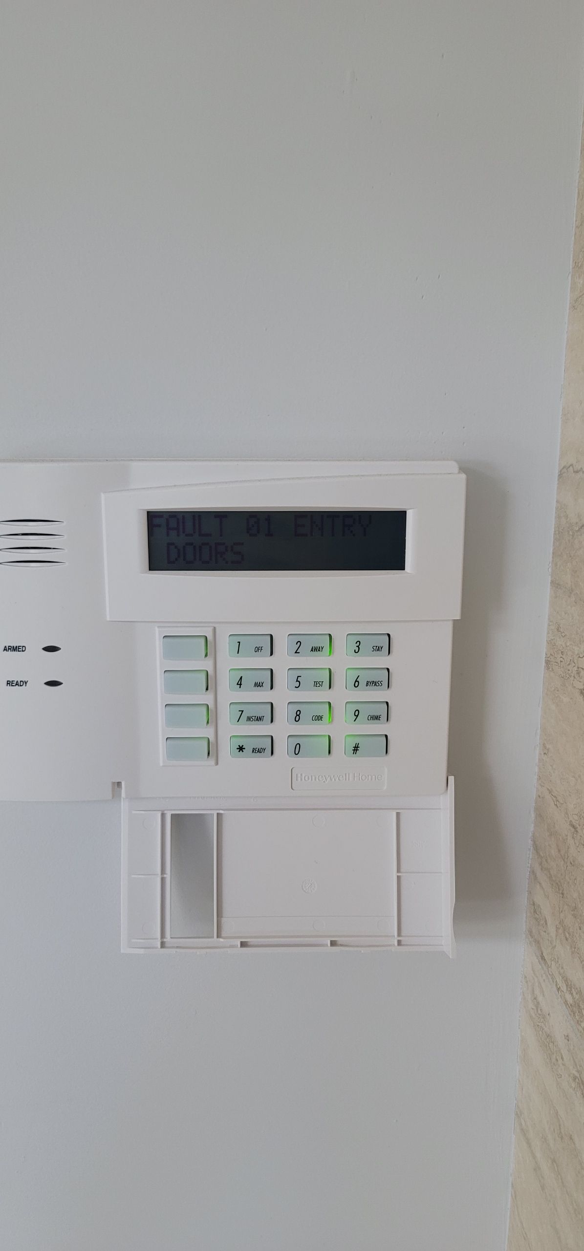 A white alarm system is hanging on a white wall.