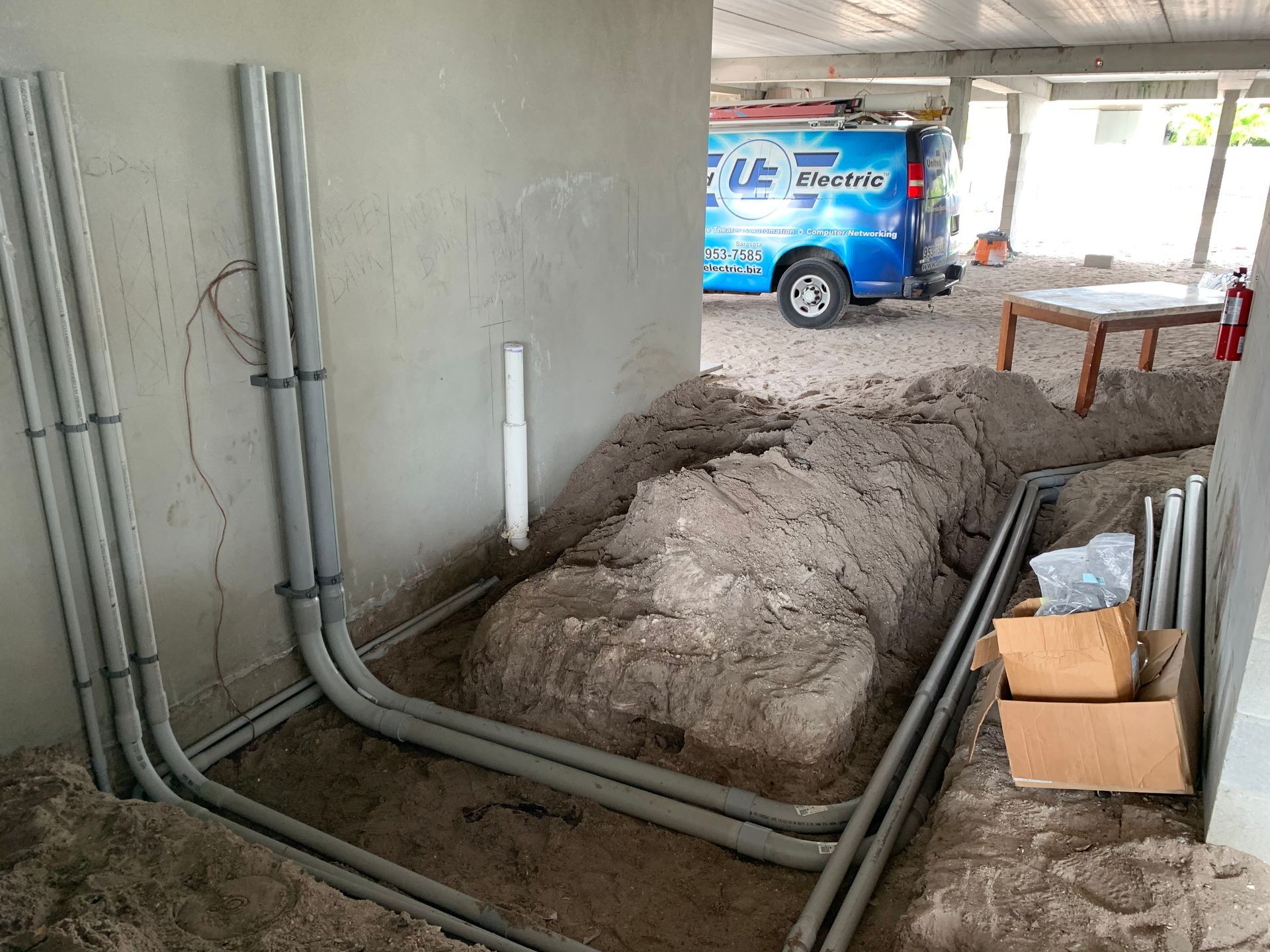 A blue van is parked in a garage next to a pile of pipes.