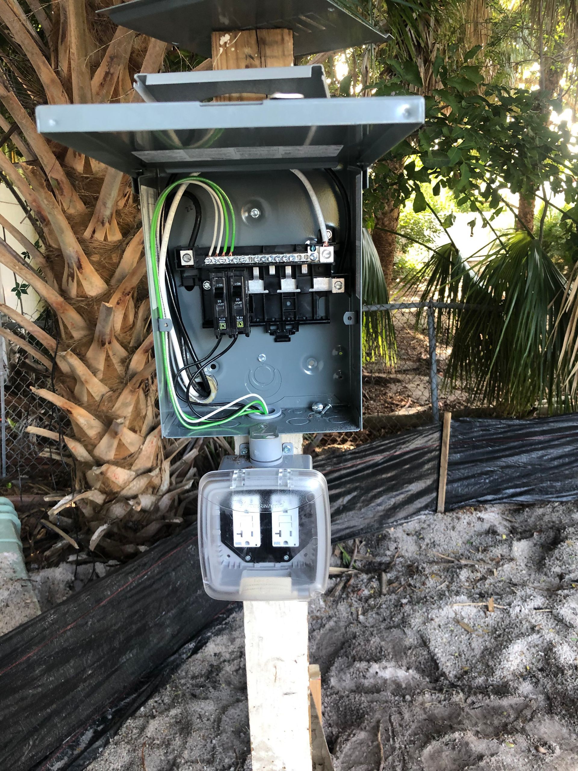 A electrical box is sitting on top of a pole in the dirt.