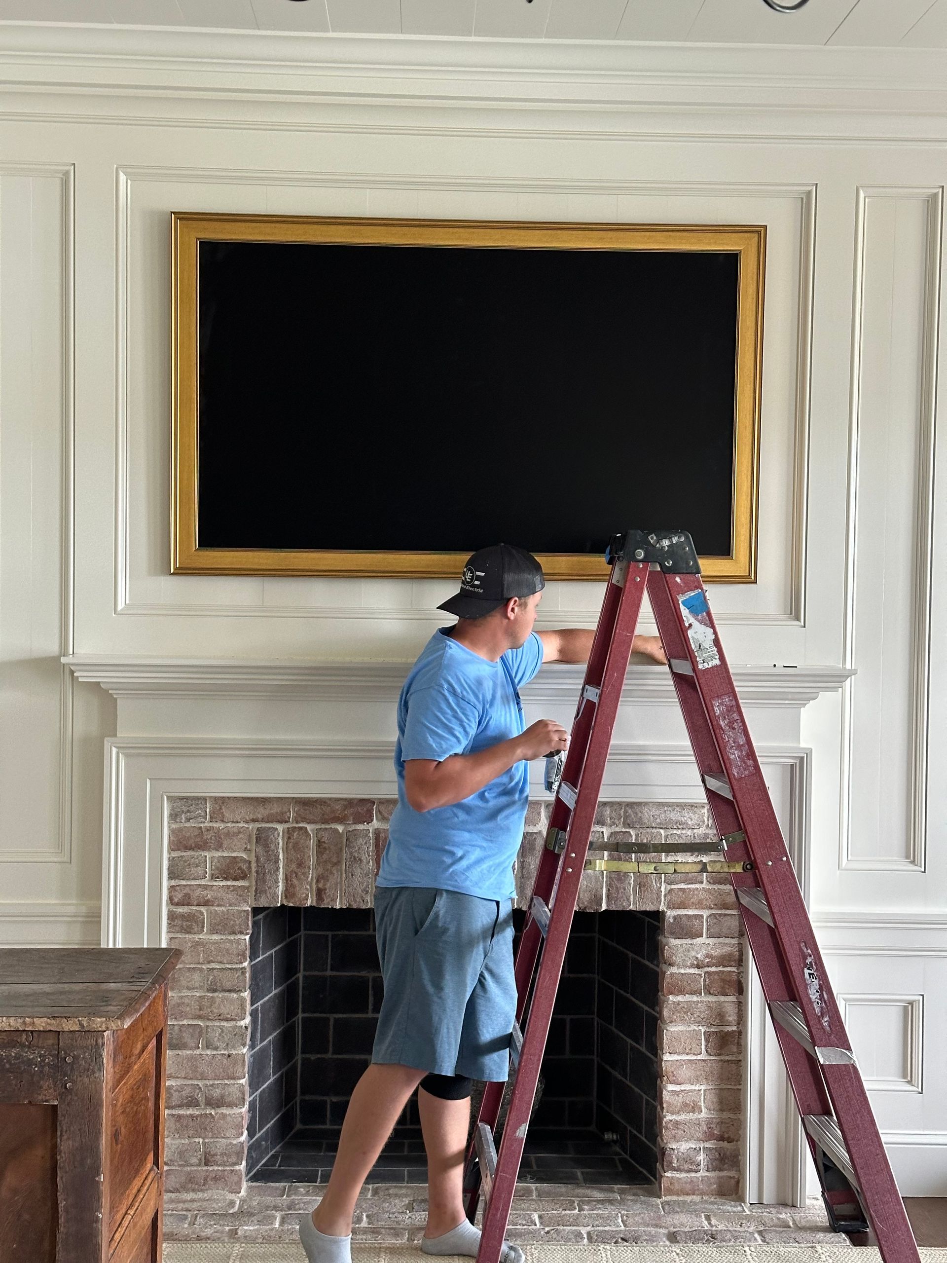 A man is standing on a ladder in front of a fireplace.