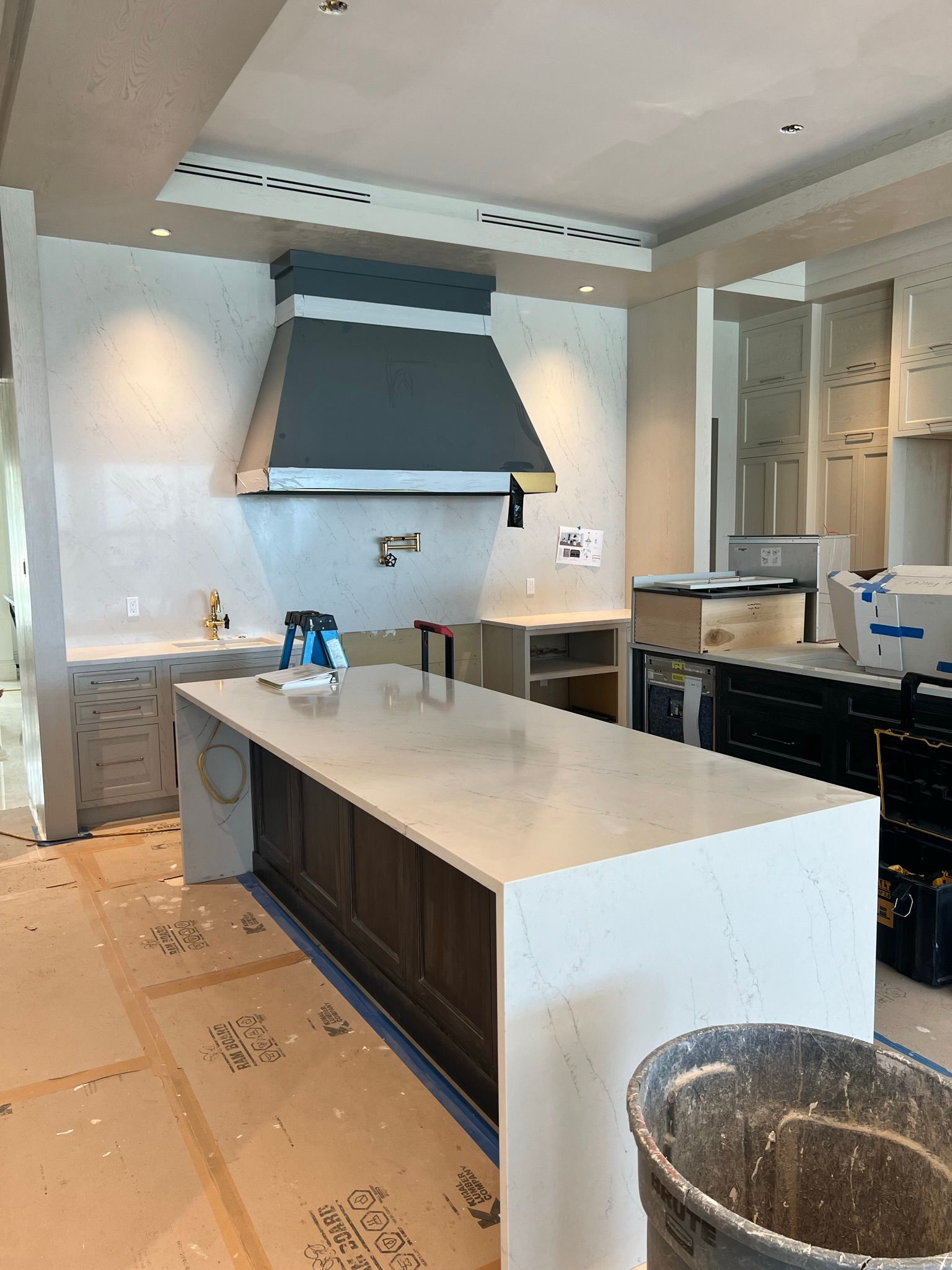 A kitchen under construction with a large island and a hood.