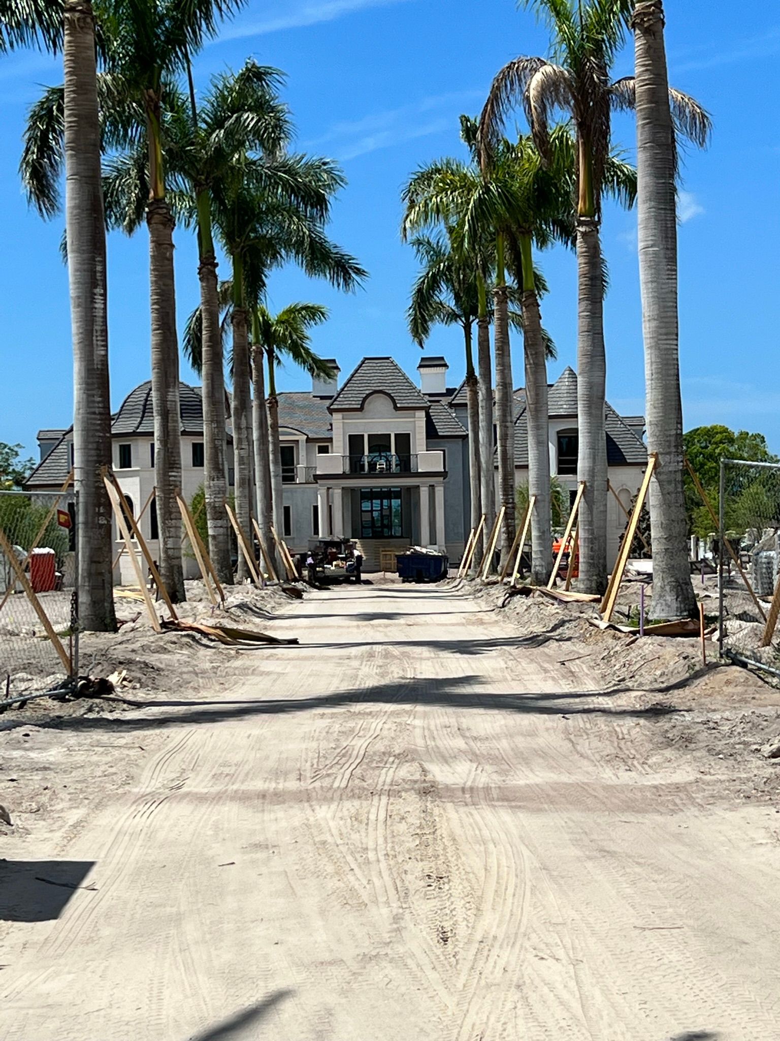 A dirt road leads to a large house surrounded by palm trees