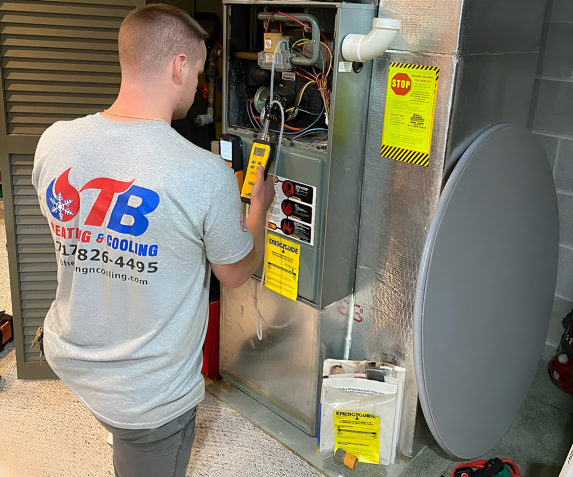 HVAC technician in gray shirt using a multimeter on furnace