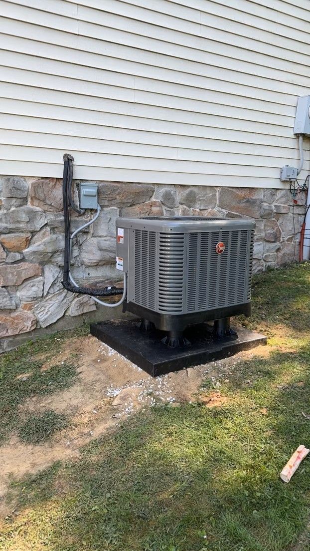 An air conditioner is sitting on top of a concrete platform in front of a house.