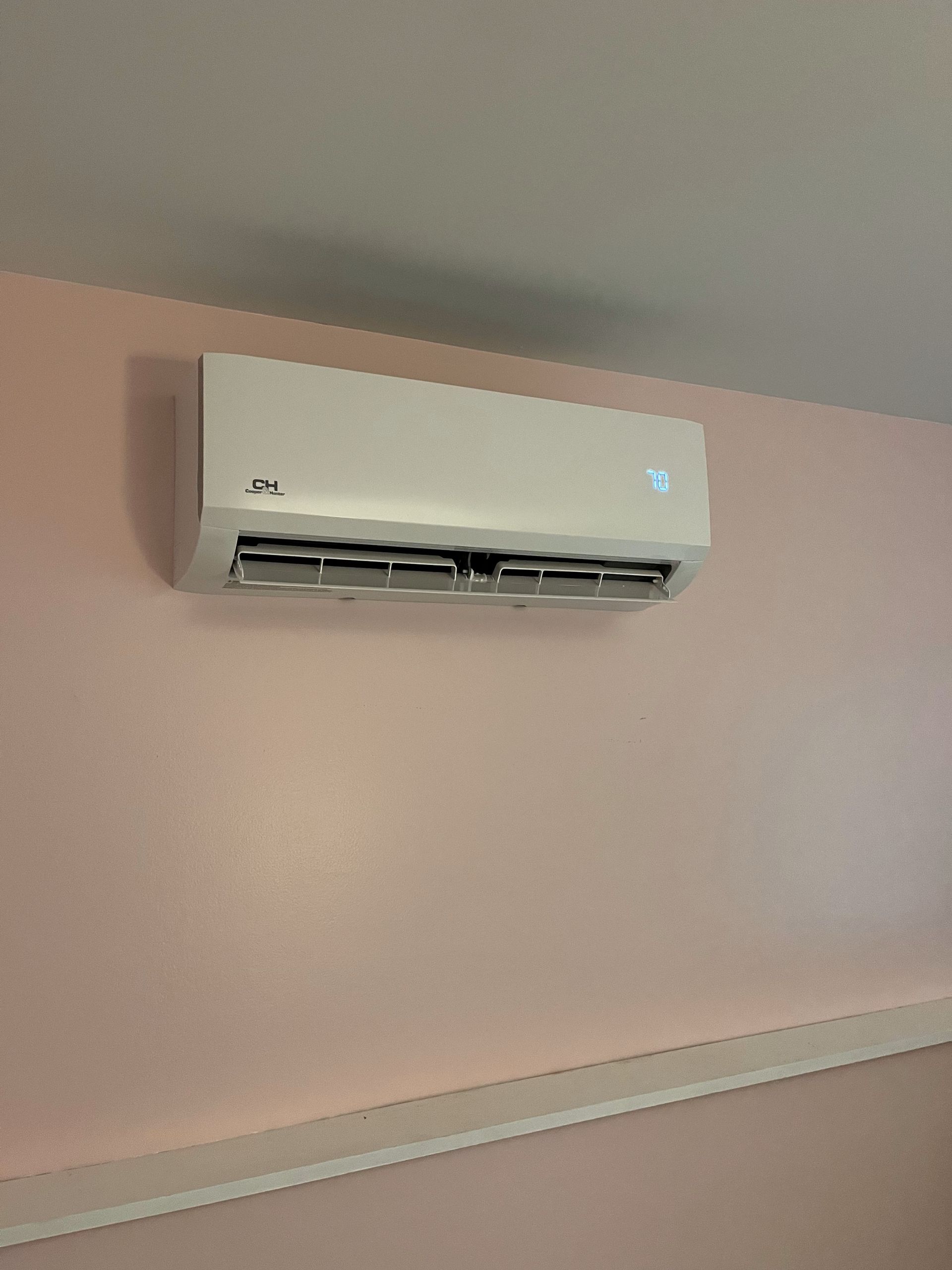 A white air conditioner is hanging on a pink wall.