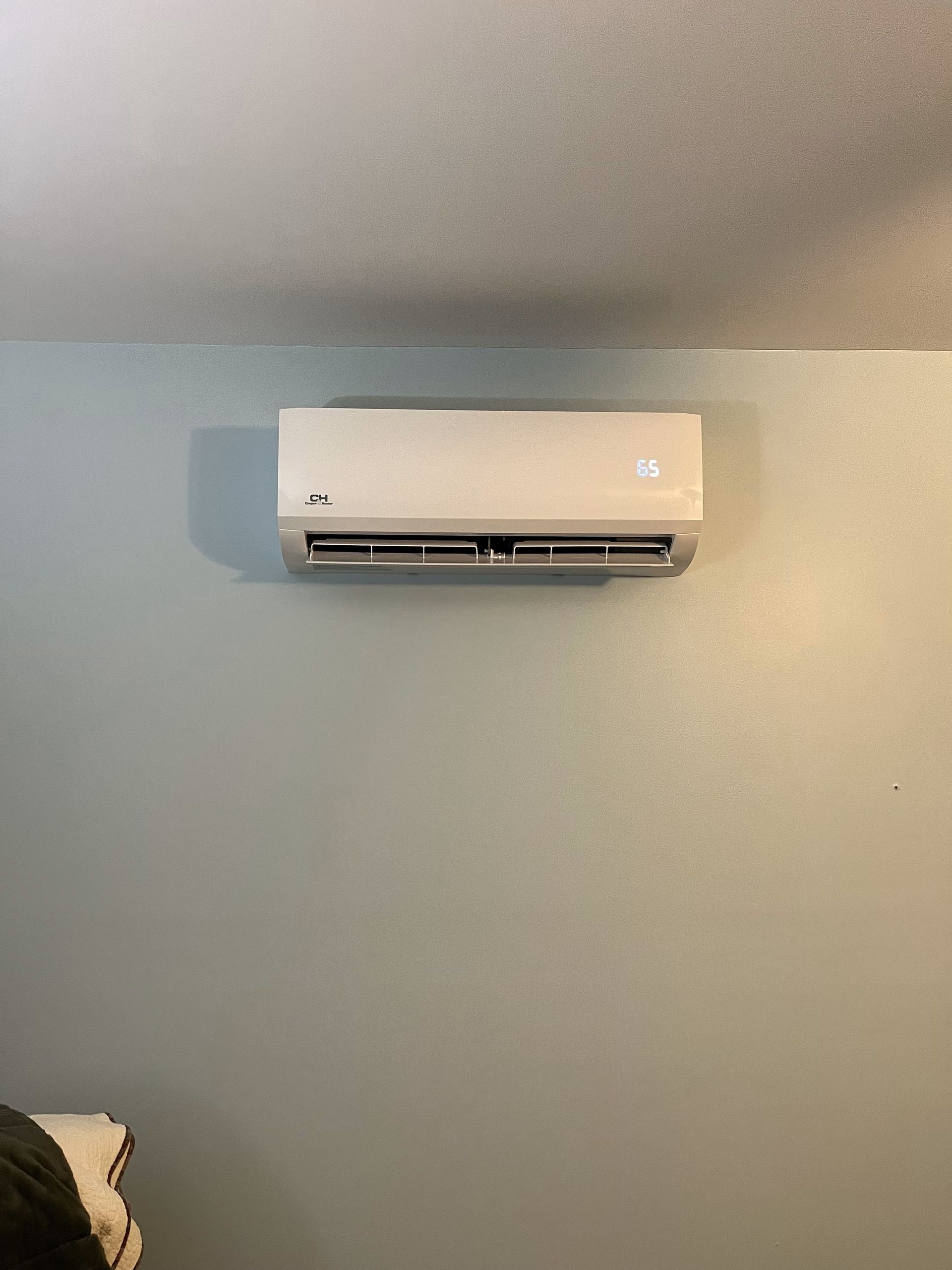 A white air conditioner is hanging on a wall in a bedroom.