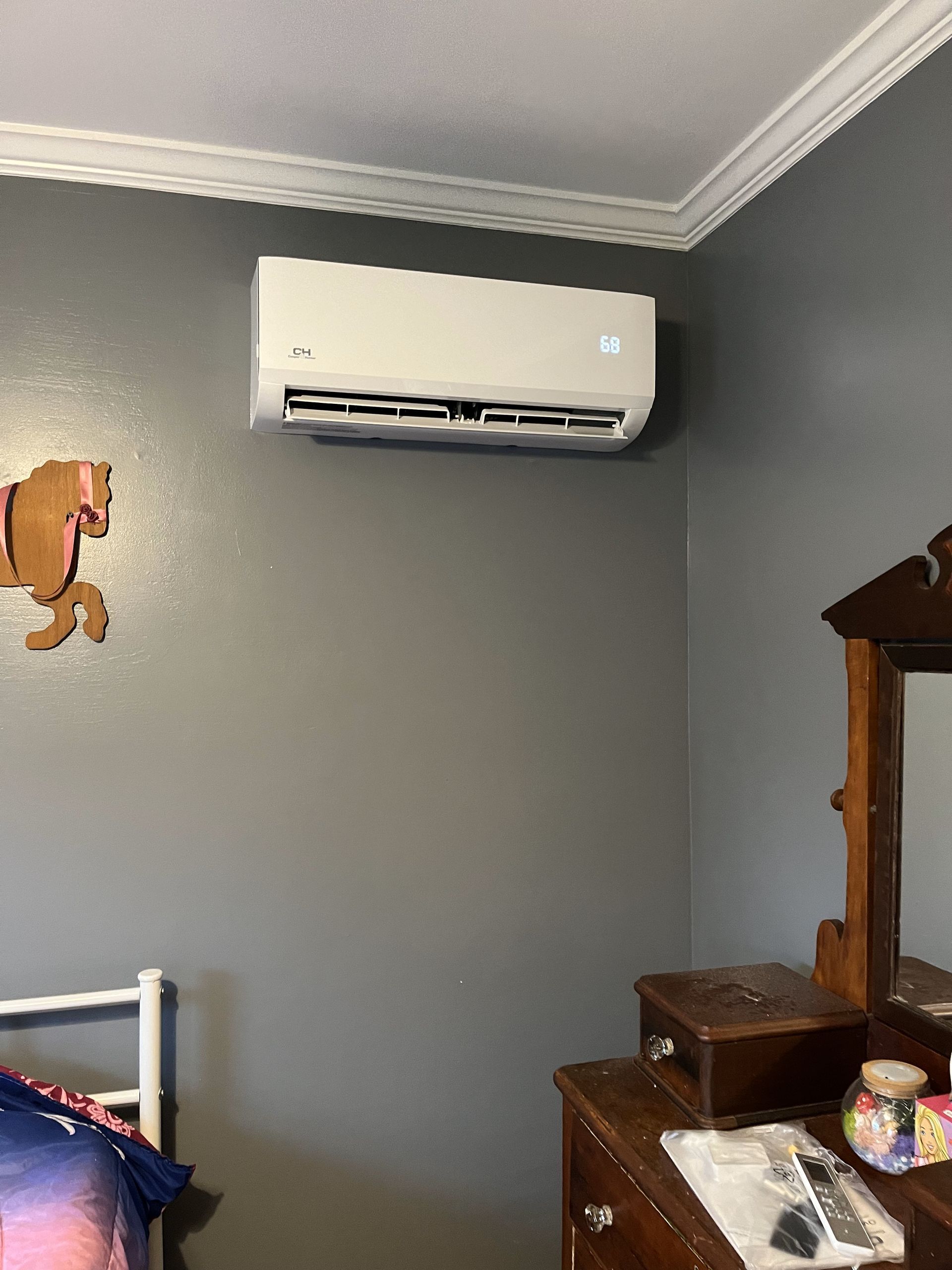 A bedroom with a bed , dresser , mirror and air conditioner on the wall.