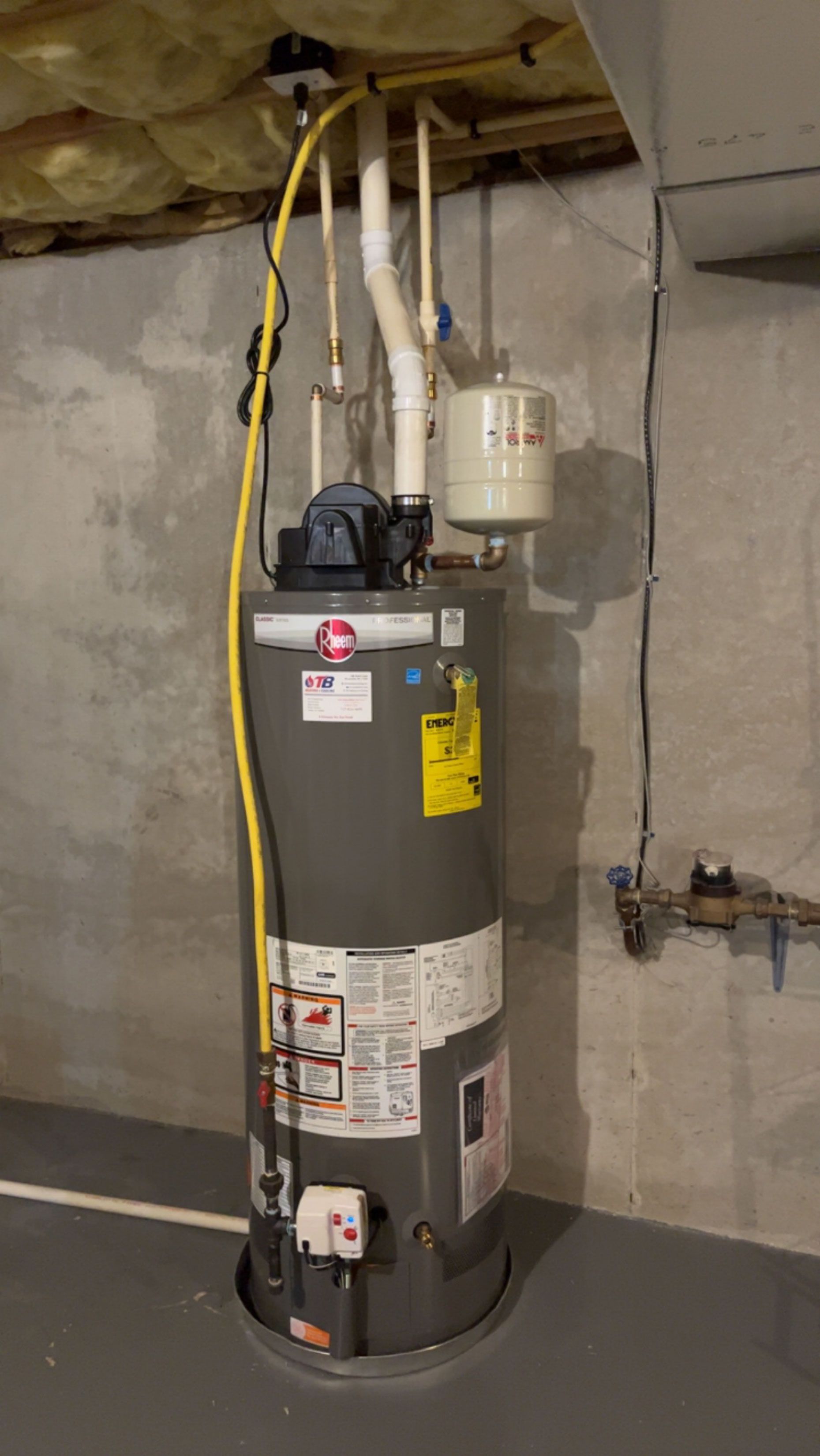A water heater is sitting in a basement next to a wall.