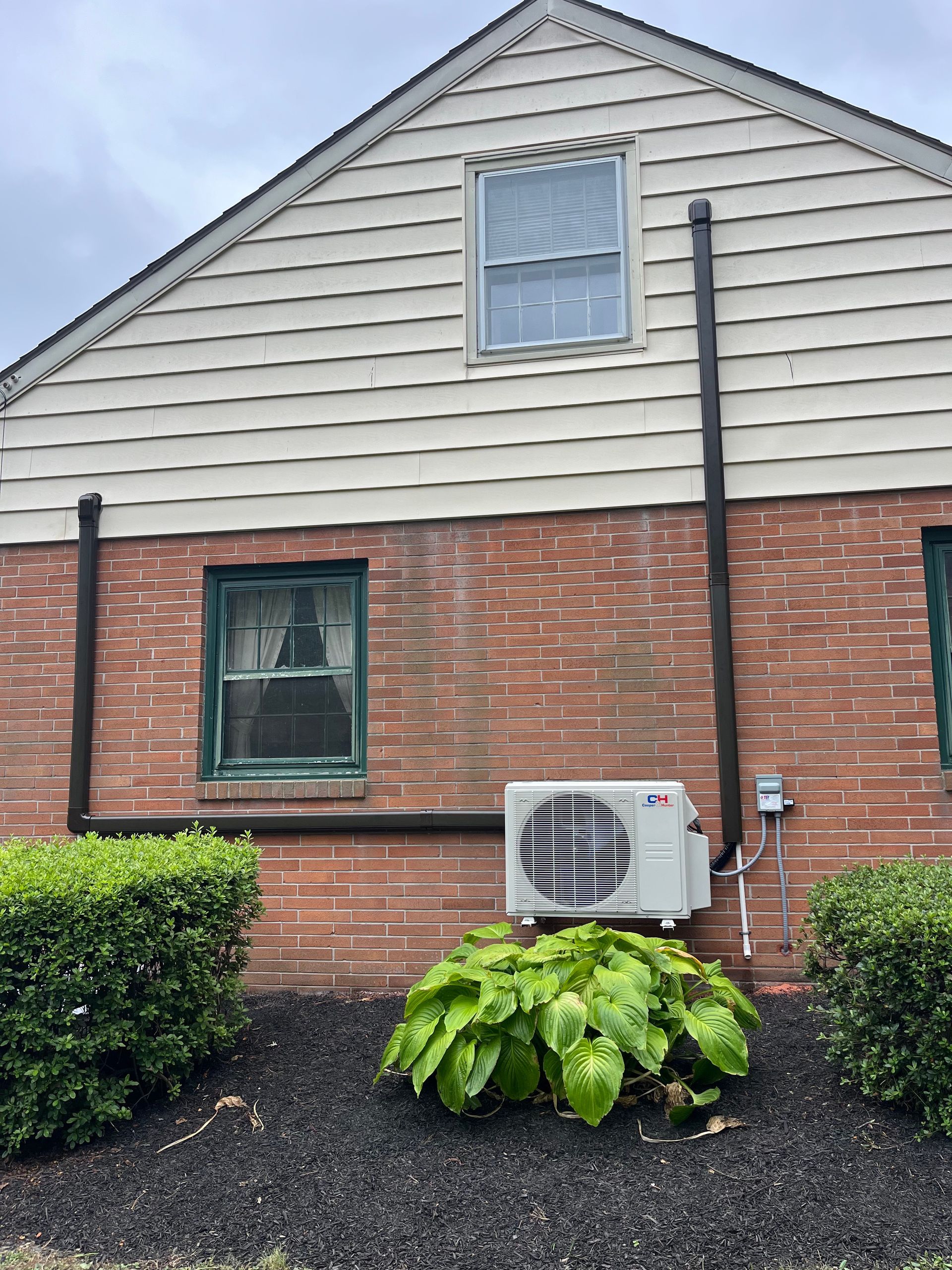 A brick house with a white siding and a white air conditioner on the side of it.