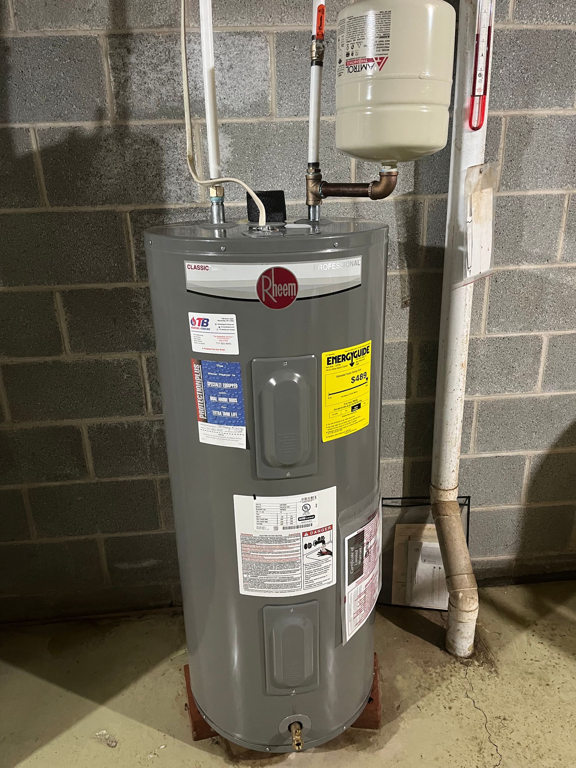 A gray water heater is sitting in a basement next to a brick wall.