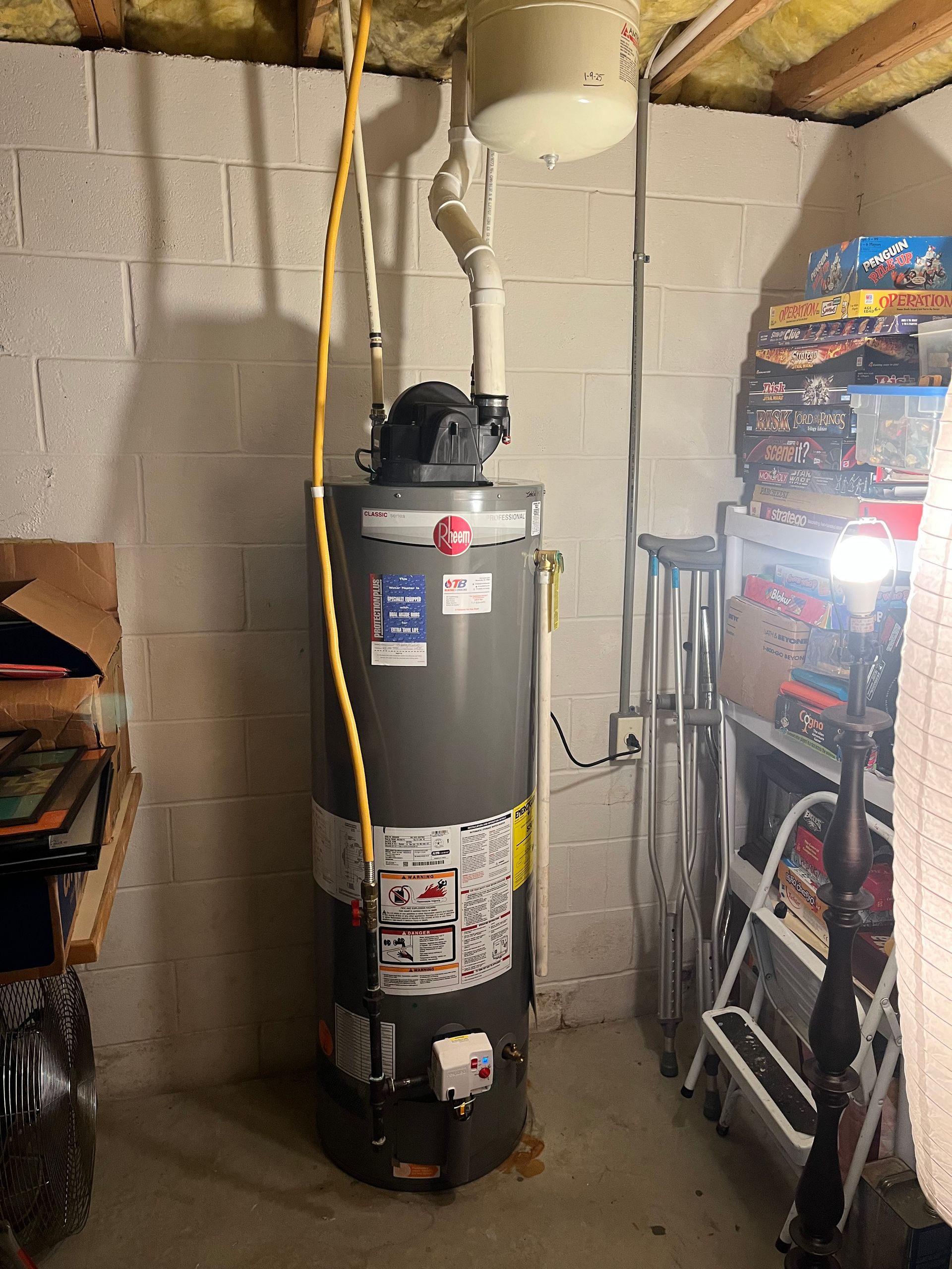 A water heater is sitting in a basement next to a ladder.