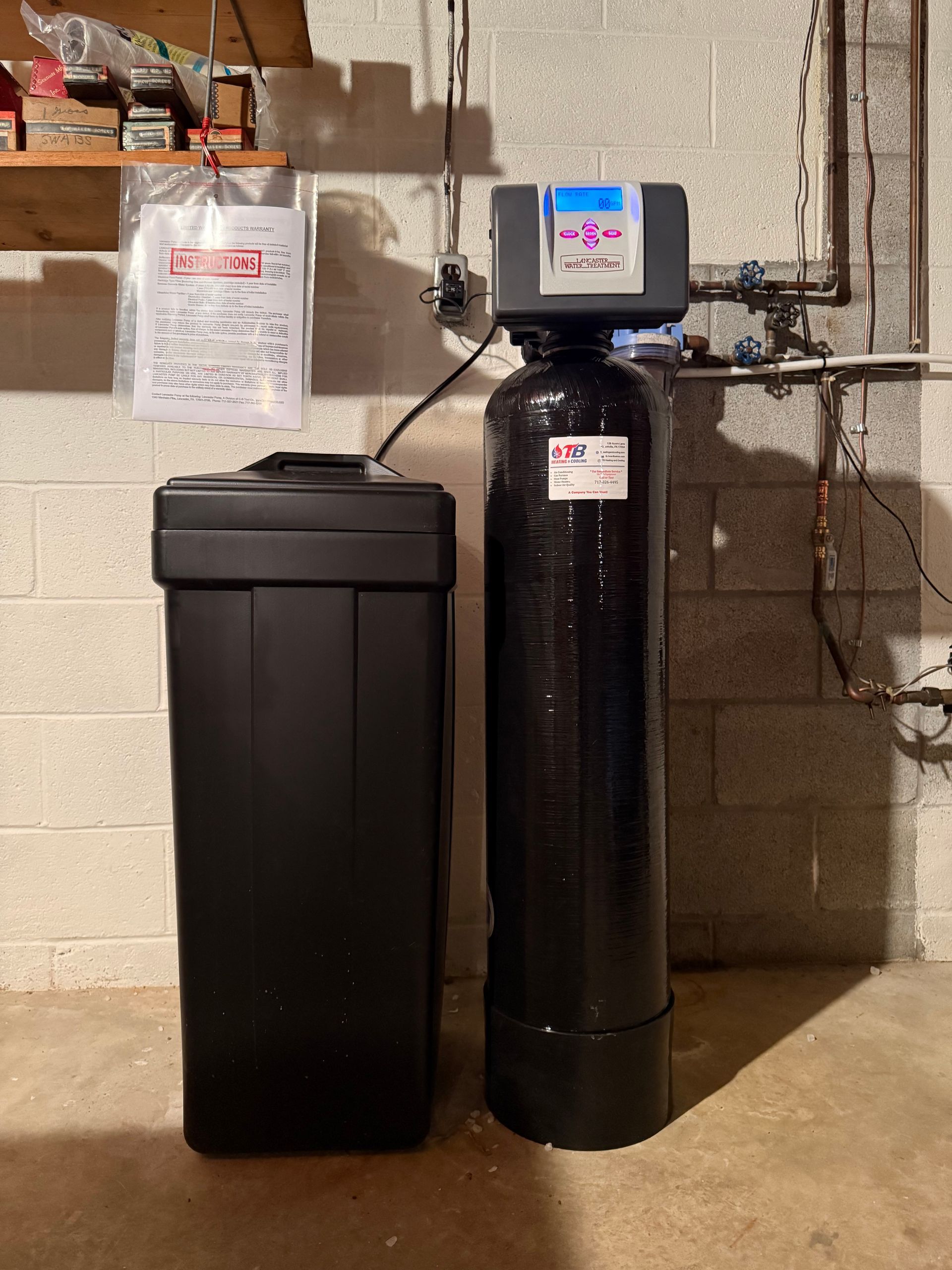 A water softener is sitting next to a water tank in a basement.