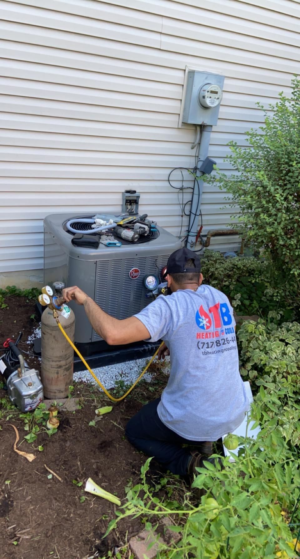 A man is working on an air conditioner outside of a house.