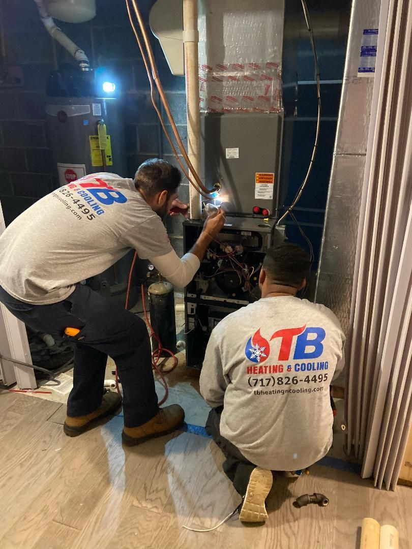 Two men are working on a furnace in a room.