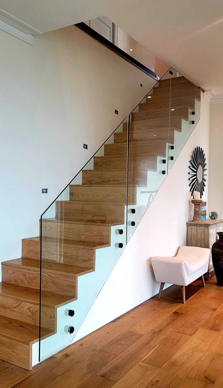 a wooden staircase with a glass railing in a living room.