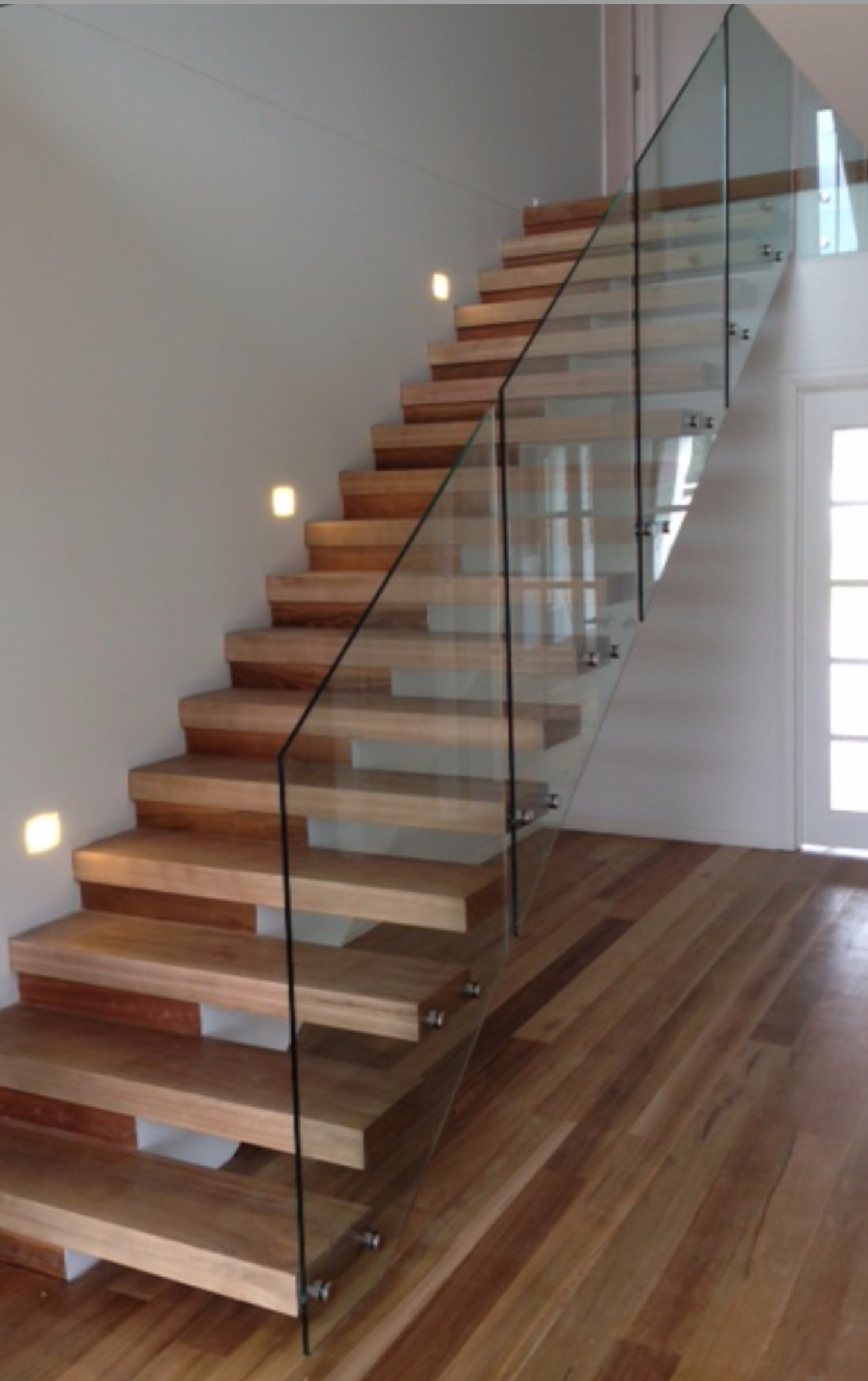 a wooden staircase with a clear glass railing.
