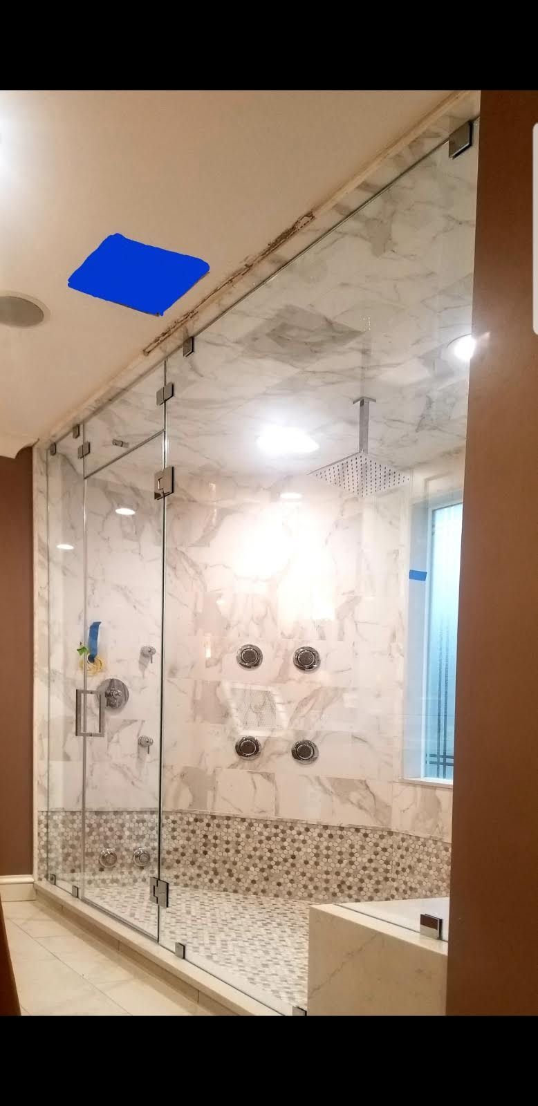 a bathroom with a glass shower door and a blue square on the ceiling.