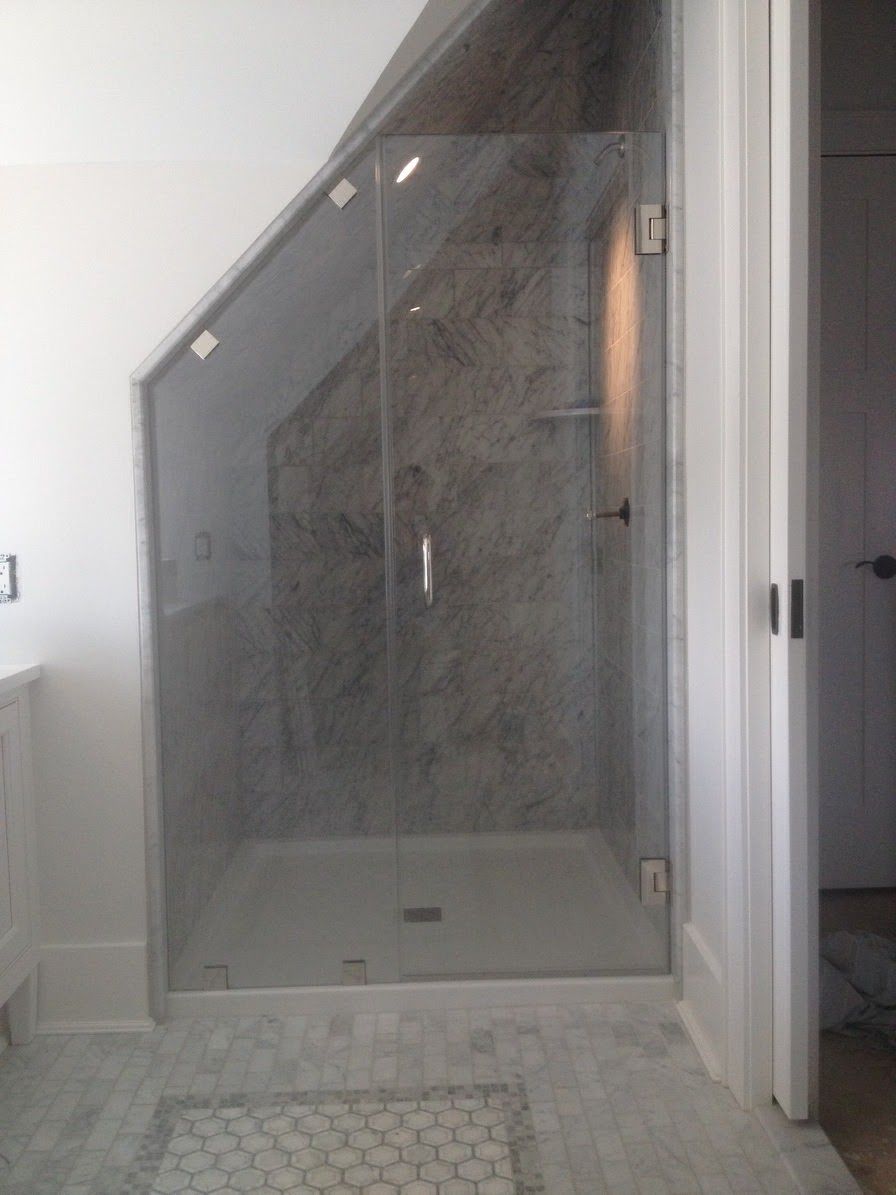 a bathroom with a glass shower door under a slanted ceiling.