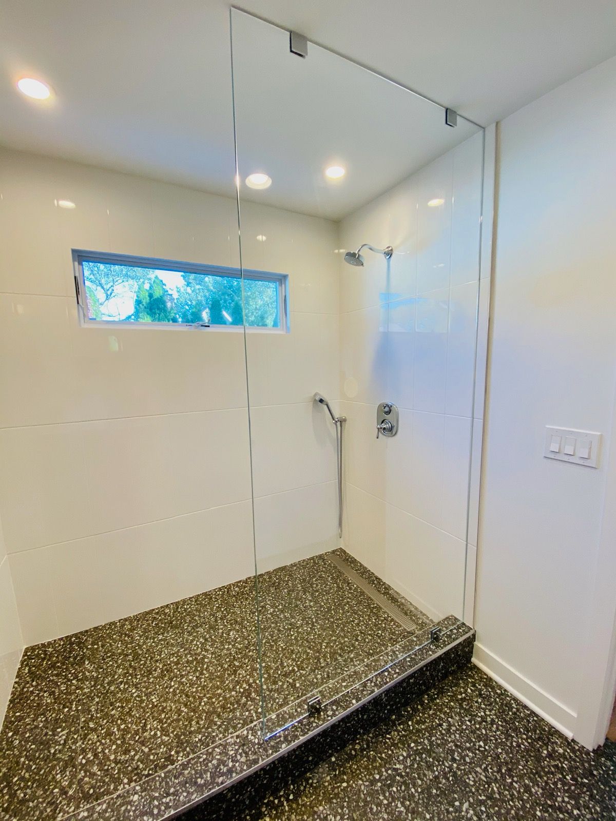 a bathroom with a walk in shower with a glass door and a window.