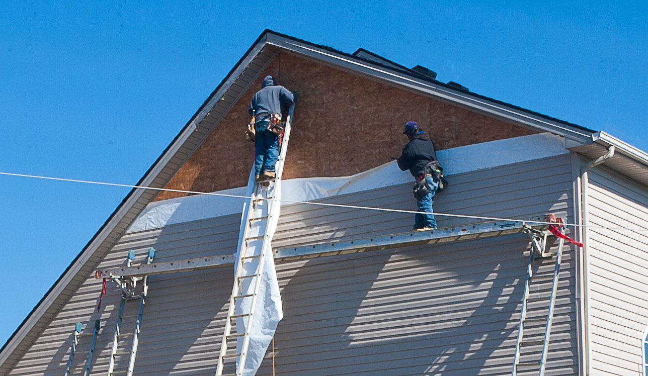 Workers on a house roof installing siding under a blue sky