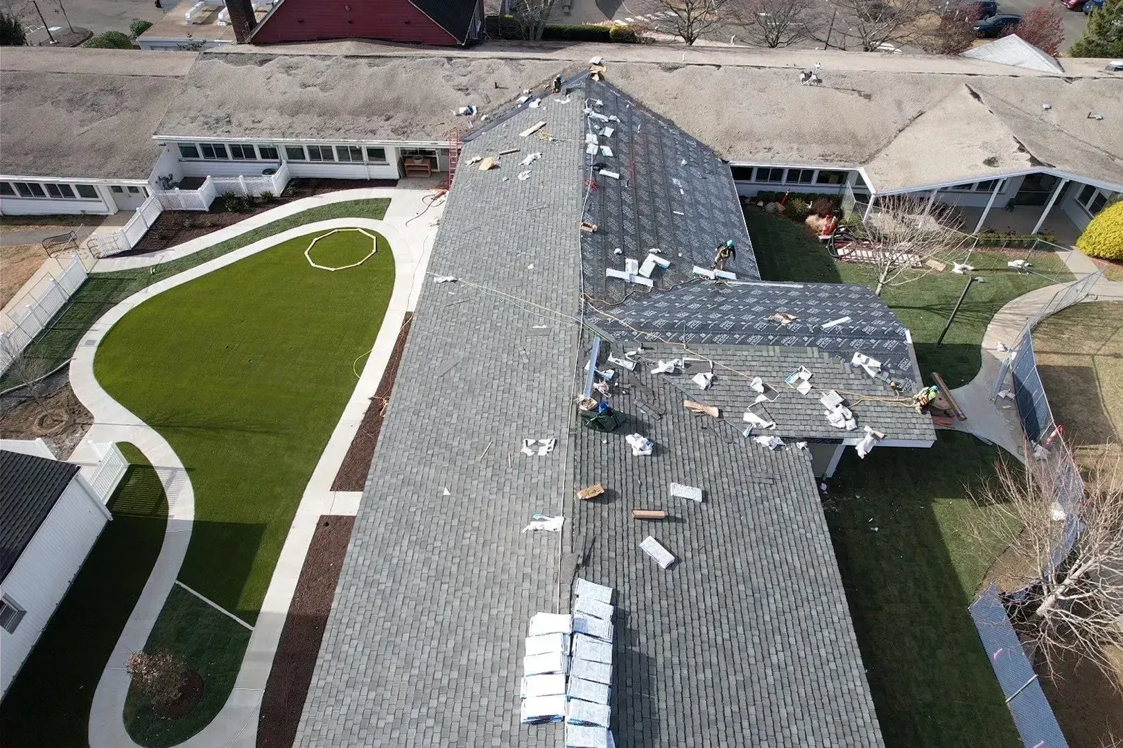 Aerial view of a damaged roof with missing shingles and debris beside a curved walkway and green lawn