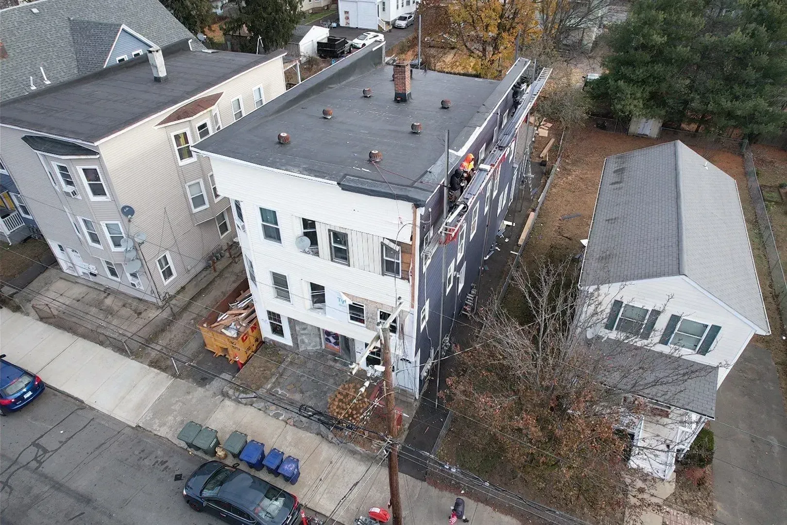 Aerial view of a white three-story building on a residential street, with parked cars and nearby trees.