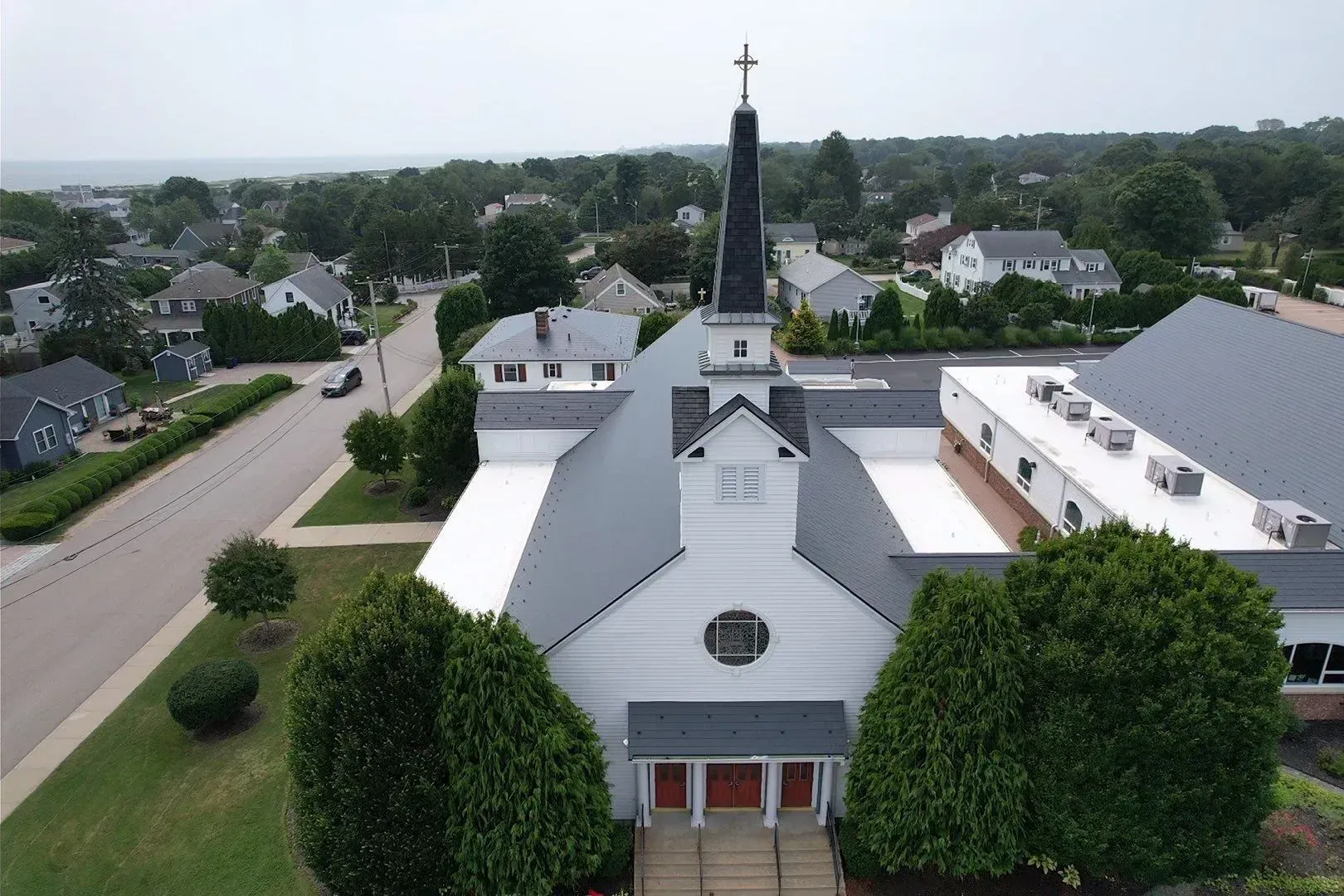 Aerial view of a white church with a tall steeple in a suburban neighborhood.