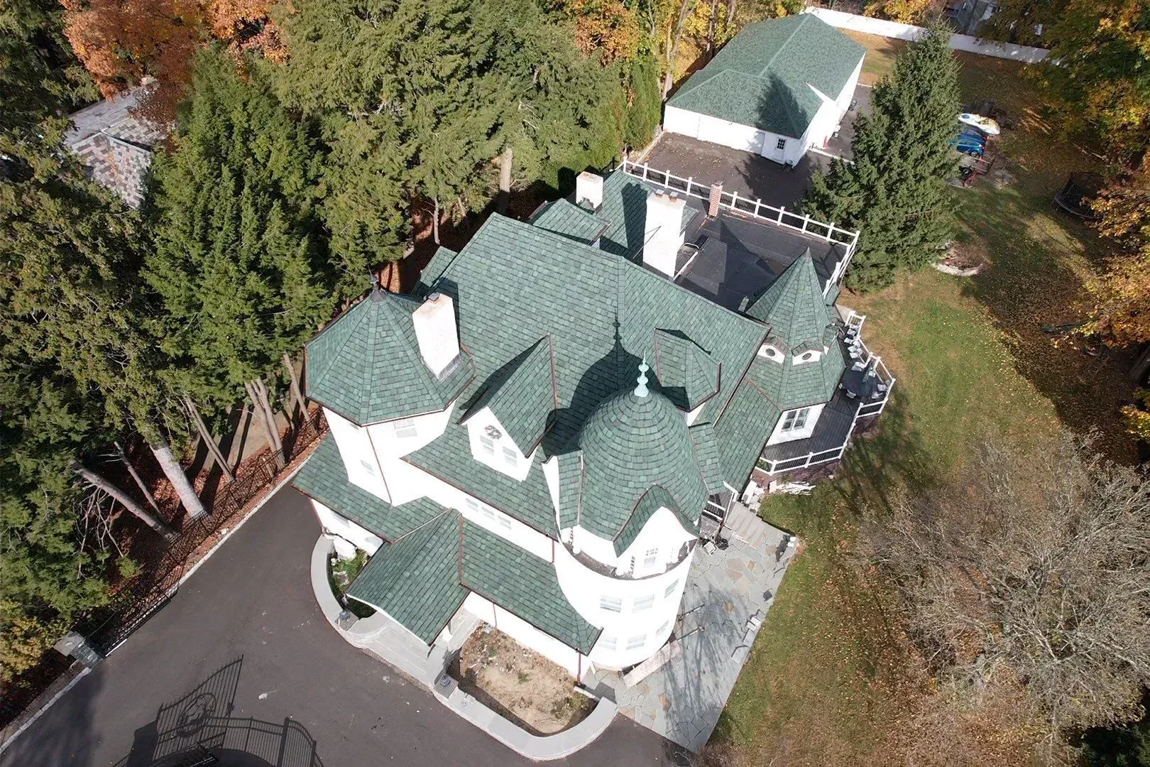Aerial view of a white house with a green roof surrounded by trees and a driveway