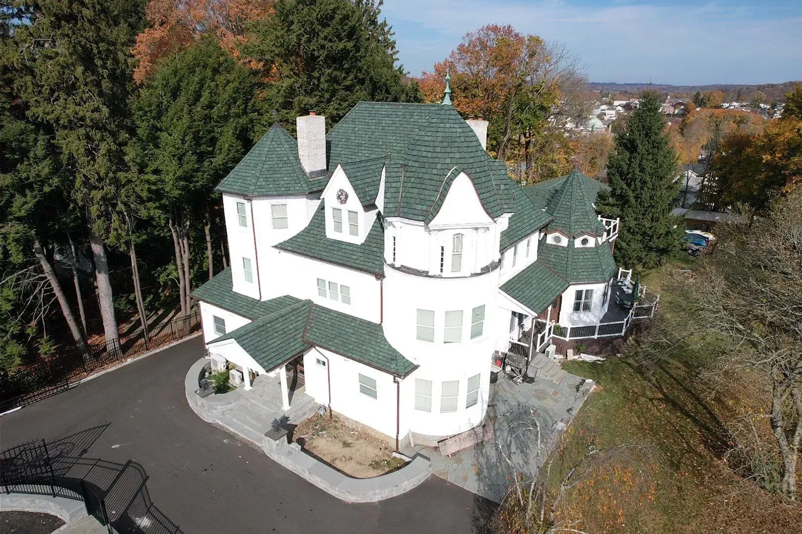Aerial view of a white house with a green roof surrounded by trees in autumn.