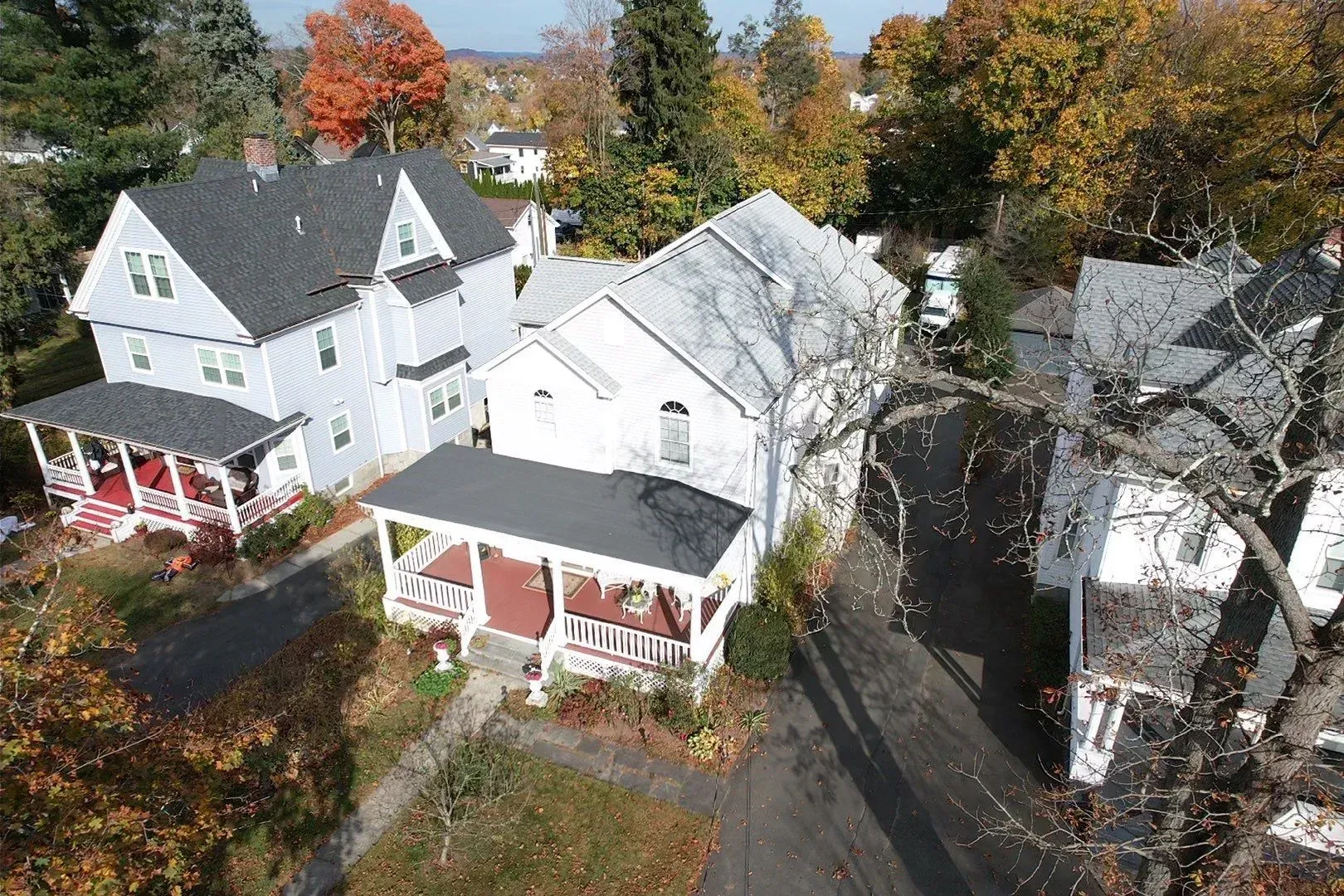 Aerial view of white houses with porches on a tree-lined residential street in autumn