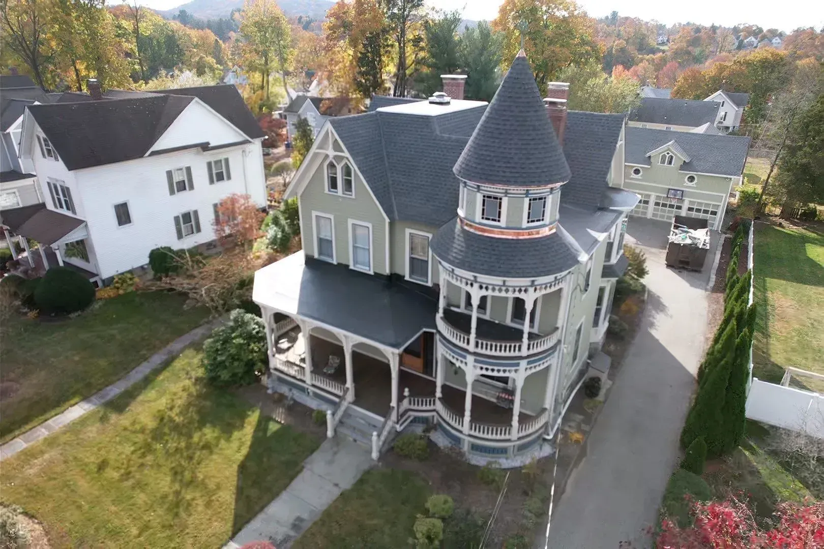 Victorian-style house with turret and wraparound porch in a leafy neighborhood, seen from above