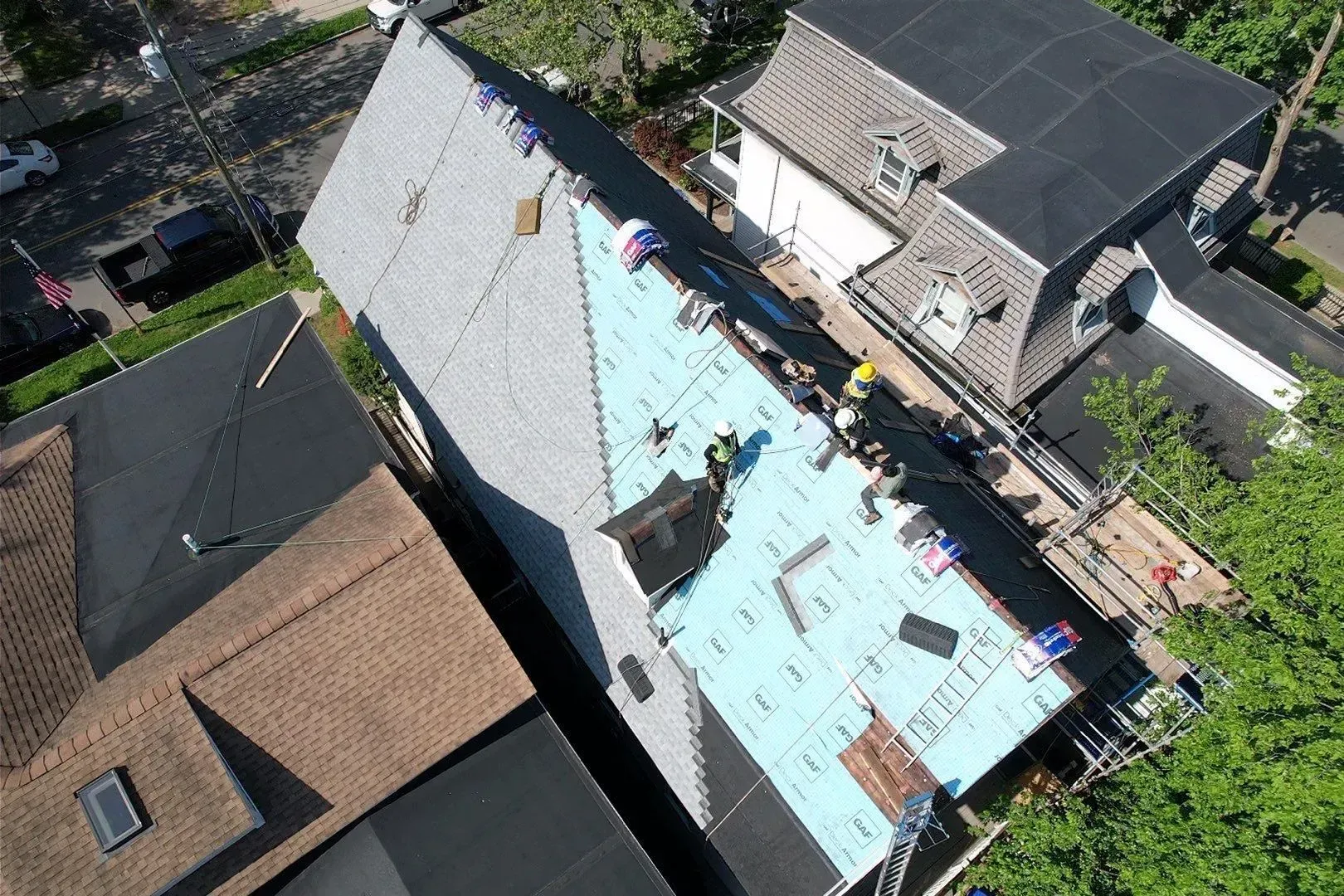 Aerial view of a house roof under repair, with blue tarp and roofing materials nearby