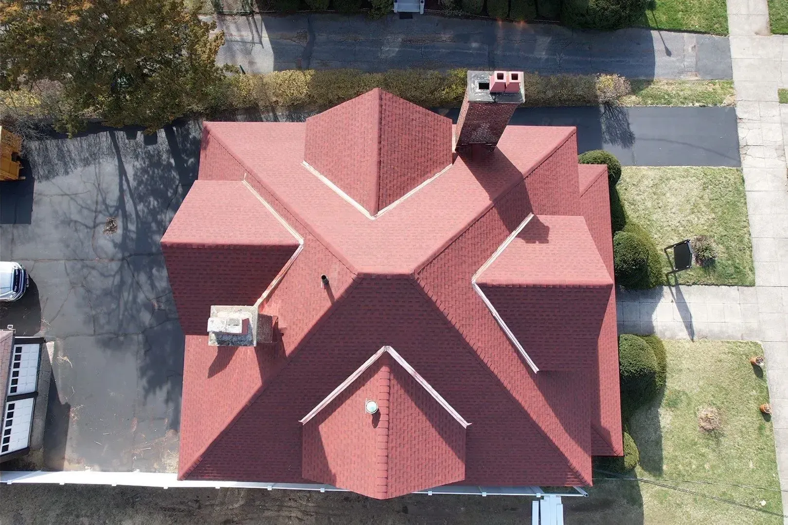 Aerial view of a red-roofed house with a chimney, surrounded by a yard and neighboring sidewalks.