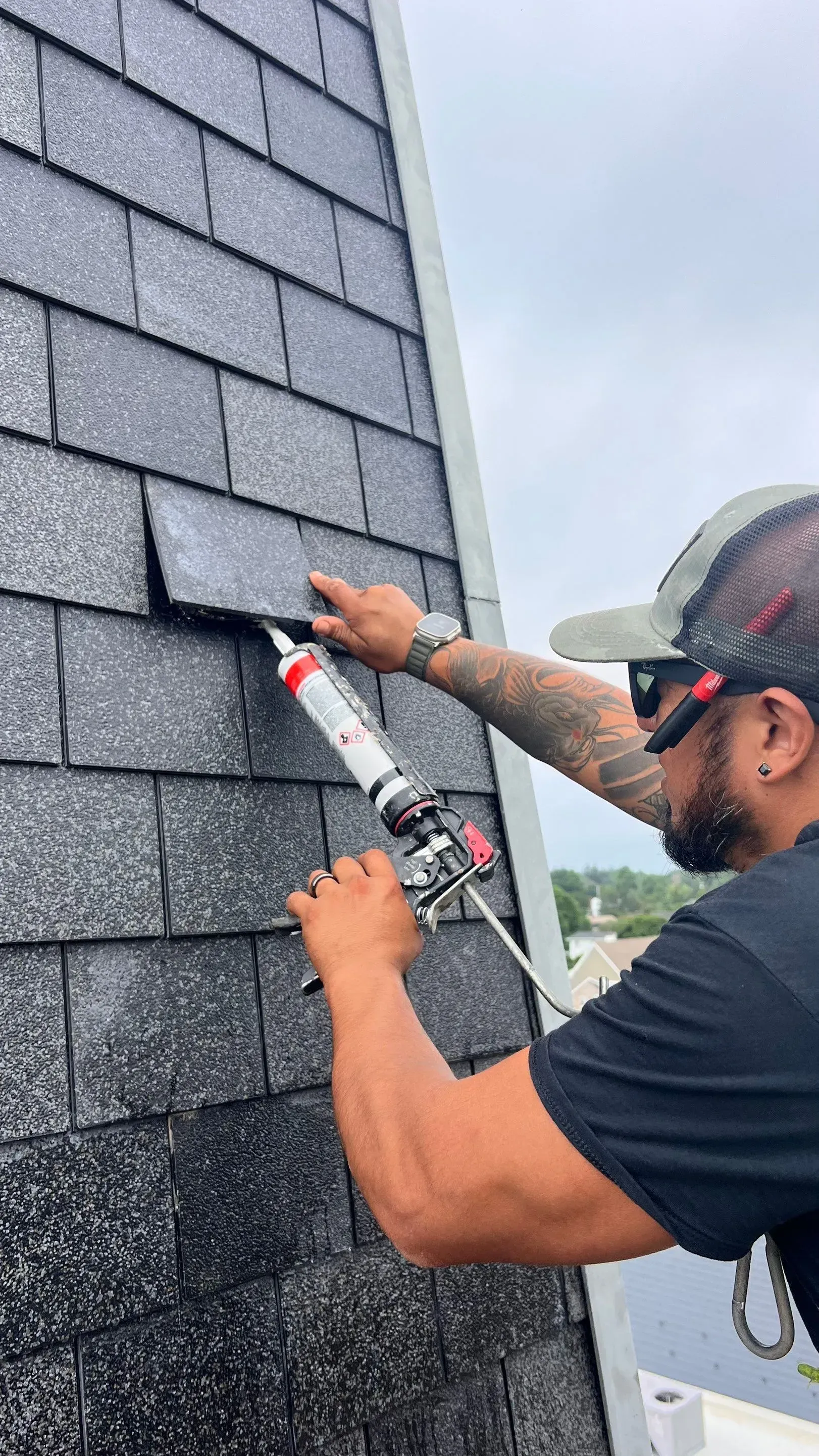 Worker caulking gray roof shingles on a house wall with a sealant gun
