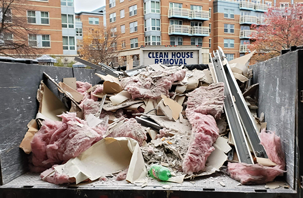 Dumpster overflowing with construction debris, including insulation, against an urban backdrop.