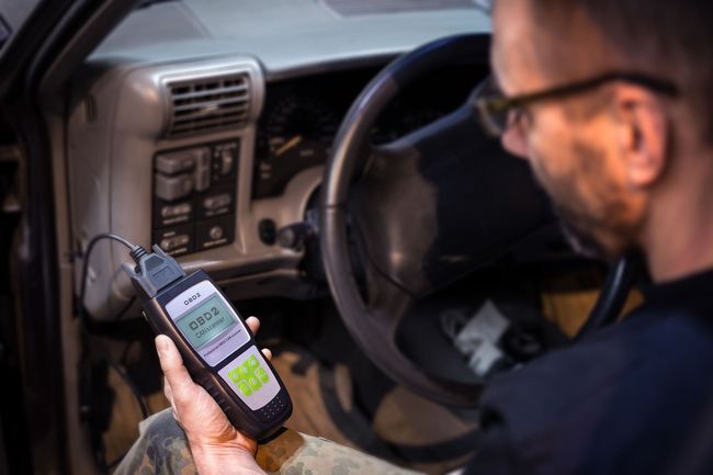 Man using an OBD2 scanner inside a car, checking for engine issues. The scanner displays readings.