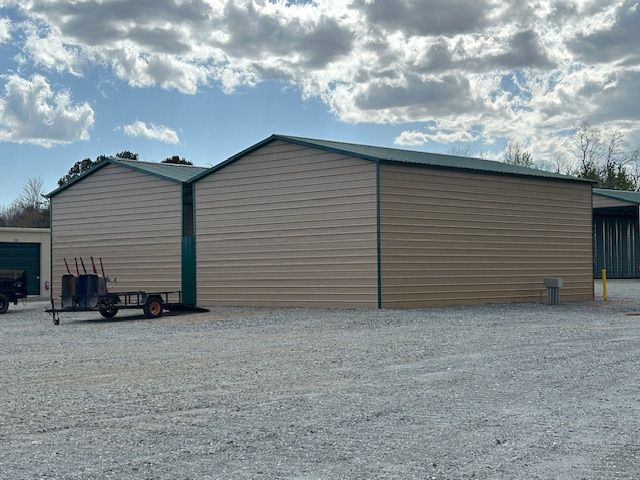 A large metal building with a green roof and a trailer parked in front of it.