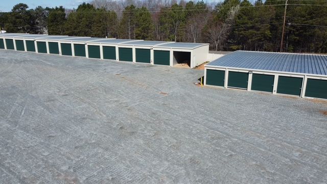 A row of green storage units are lined up in a parking lot.