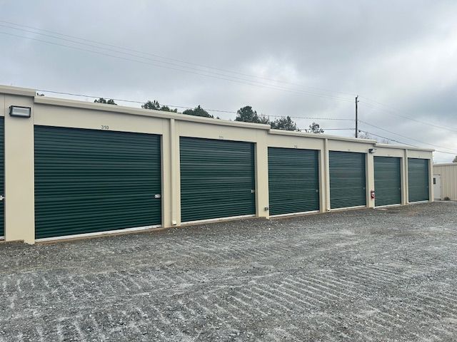 A row of green garage doors are lined up in a parking lot.