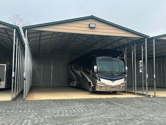 A large RV is parked under a metal building.