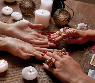 Two women are sitting at a table with candles and rings on their hands