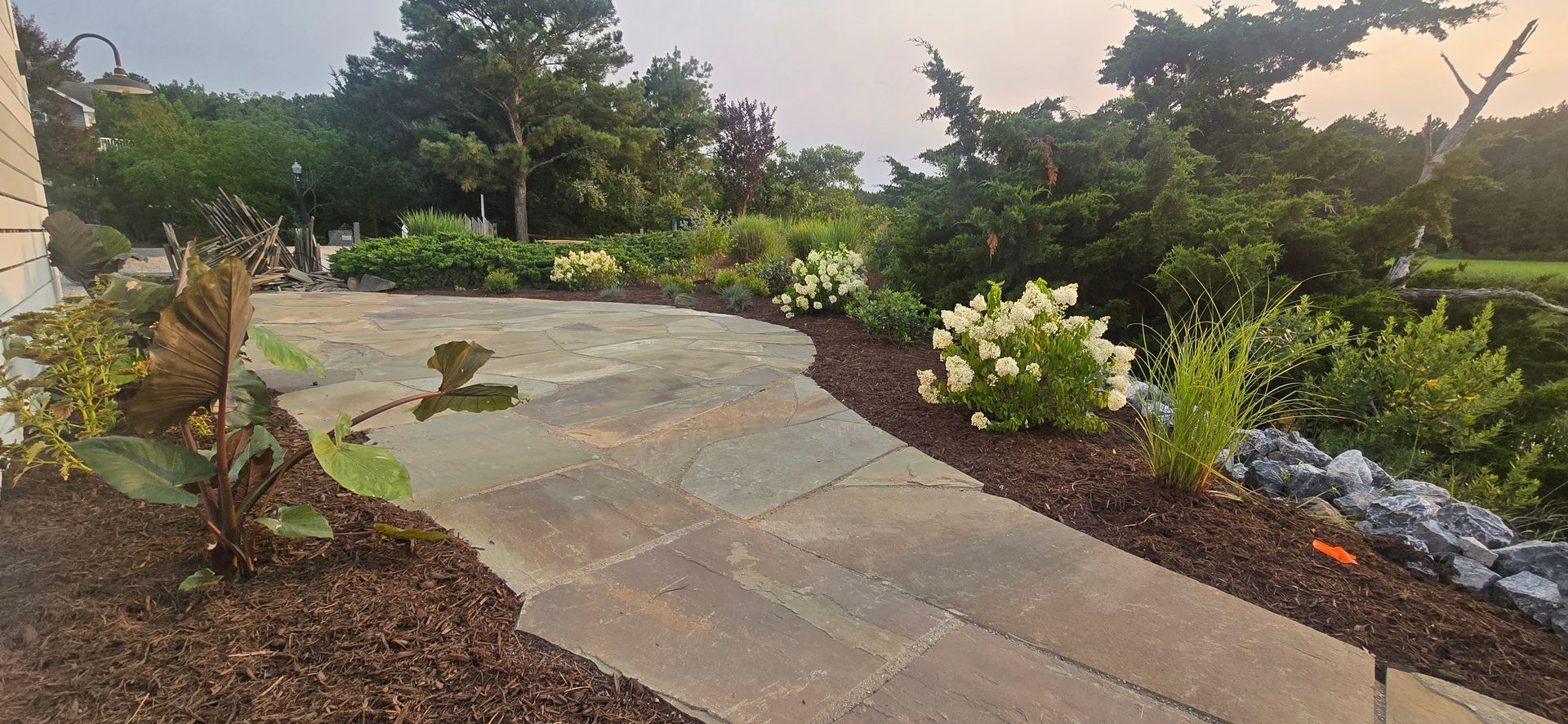 Curved stone path through a landscaped garden with shrubs, flowers, and mulch