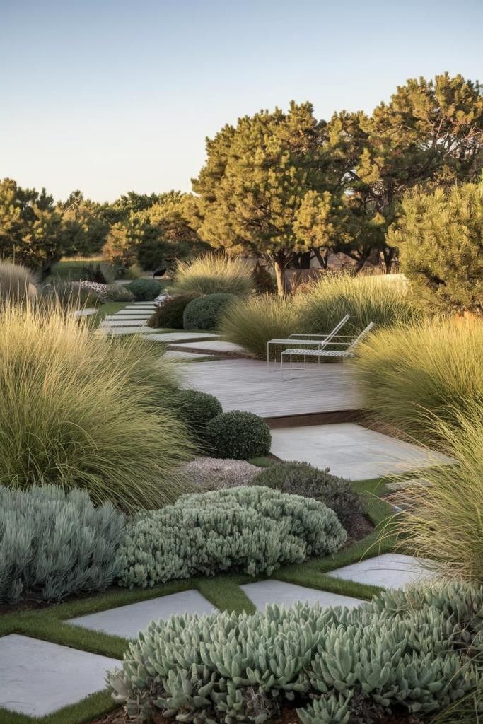 Curved stone walkway through a lush landscaped garden with grasses and shrubs at sunset