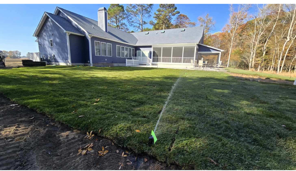 A blue house with a newly planted lawn, being watered by a sprinkler on a sunny day.