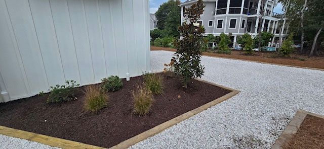 A house with a white gravel driveway and a planted garden bed next to it.