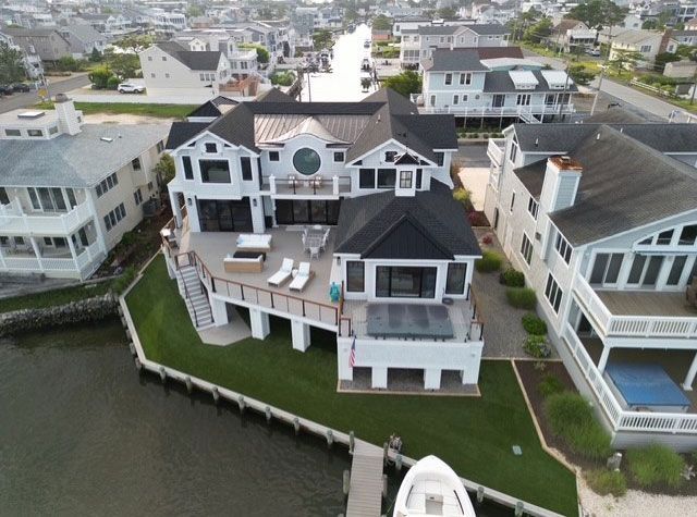 Aerial view of a large white house on a waterfront with a dock, lawn, and adjacent houses.