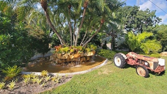 An old tractor is parked in a garden next to a fountain.