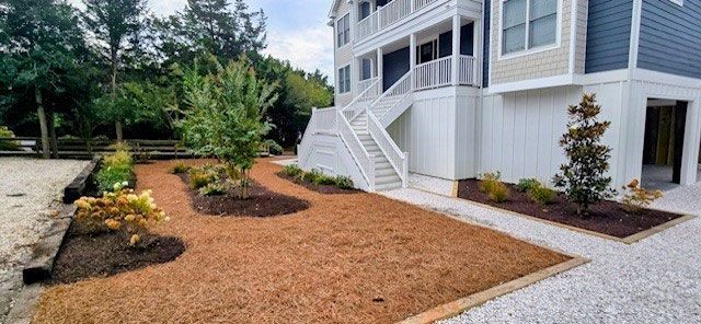 A two-story house with a white exterior, with a brown yard, landscaping, and a staircase.