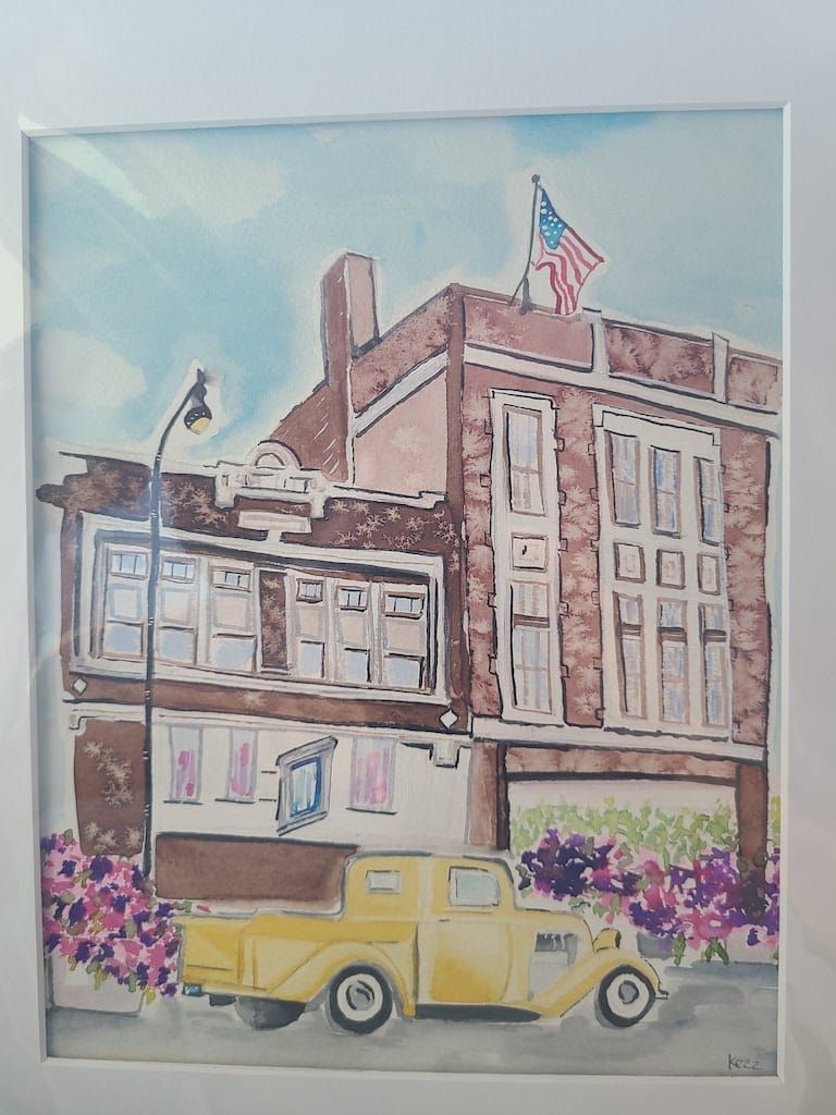 Watercolor painting of a brick building with an American flag, yellow truck, and purple flowers.